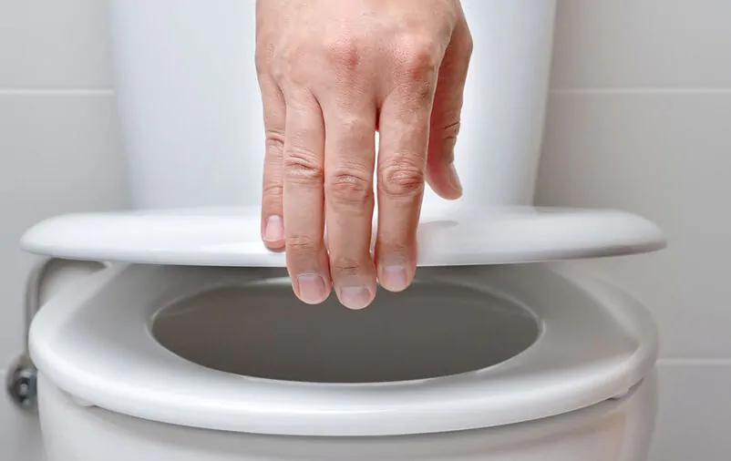 Protetor De Vaso Sanitário Descartável: Qual É A Utilidade? mão levantando tampa de assento de vaso sanitário